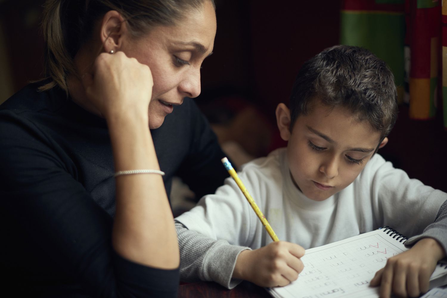 A mother sit next to her child and helps him with homework.