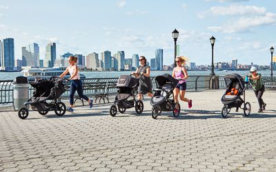 Four women running with jogging strollers with the New York City skyline in the background