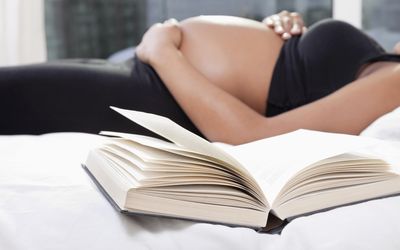 孕妇躺在床上，前景是打开的书