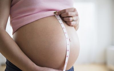 Mid section of pregnant woman measuring her belly