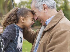 Playful grandfather and granddaughter on swing at playground laughing together