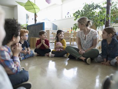 Preschool teacher and students sitting in circle on floor in classroom