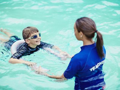 Young boy learning to swim in pool with teacher