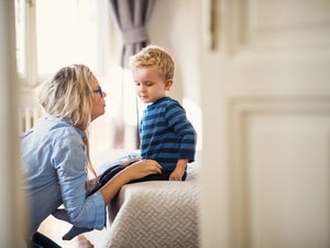 A mother talking to her toddler son inside in a bedroom