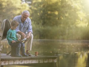 Grandfather and grandson reading at lake