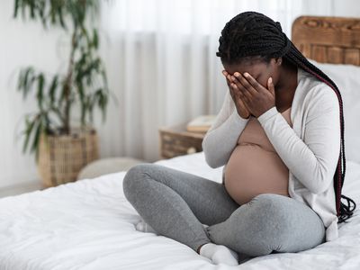 Pregnant woman sitting on bed, sad and upset