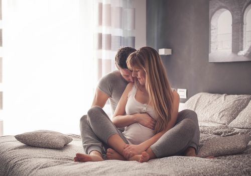 在阳光明媚的卧室里，深情的孕妇夫妇穿着睡衣在床上接吻