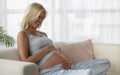 一个孕妇低头看着自己的肚子微笑着。