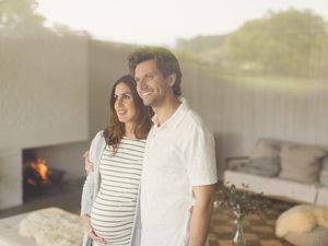 Smiling pregnant couple looking out living room window