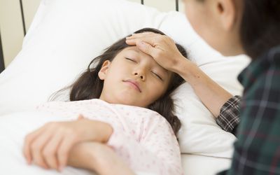 一个孩子躺在床上，父母的手放在他的额头上