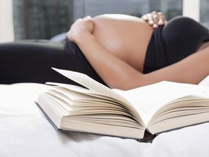 Mid section of pregnant woman lying in bed with open book in foreground