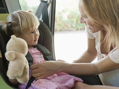 Mother fastening little girl into car seat