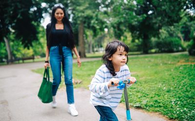 幼童骑着滑板车，妈妈在公园里看着。