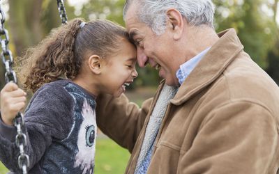 Playful grandfather and granddaughter on swing at playground laughing together