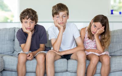 Brothers and sister on sofa looking annoyed