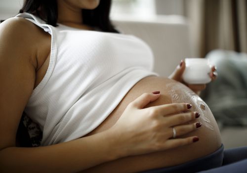 Image of a pregnant person applying a topical cream to belly.