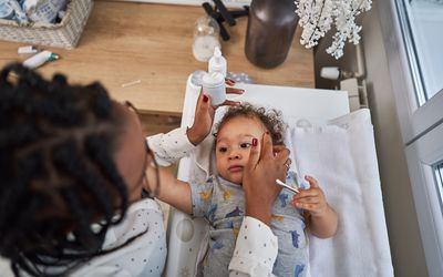 Mother applying skin lotion on her baby boy while he lying on a change bed in his nursery