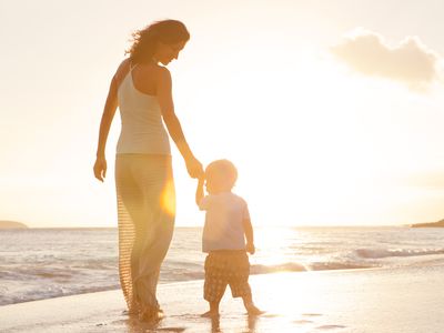 Woman in her 40s walking on beach with a child