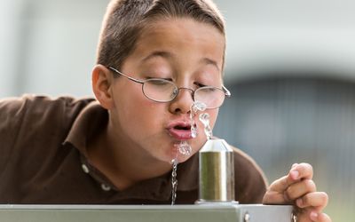 boy drinks water at school fountain.