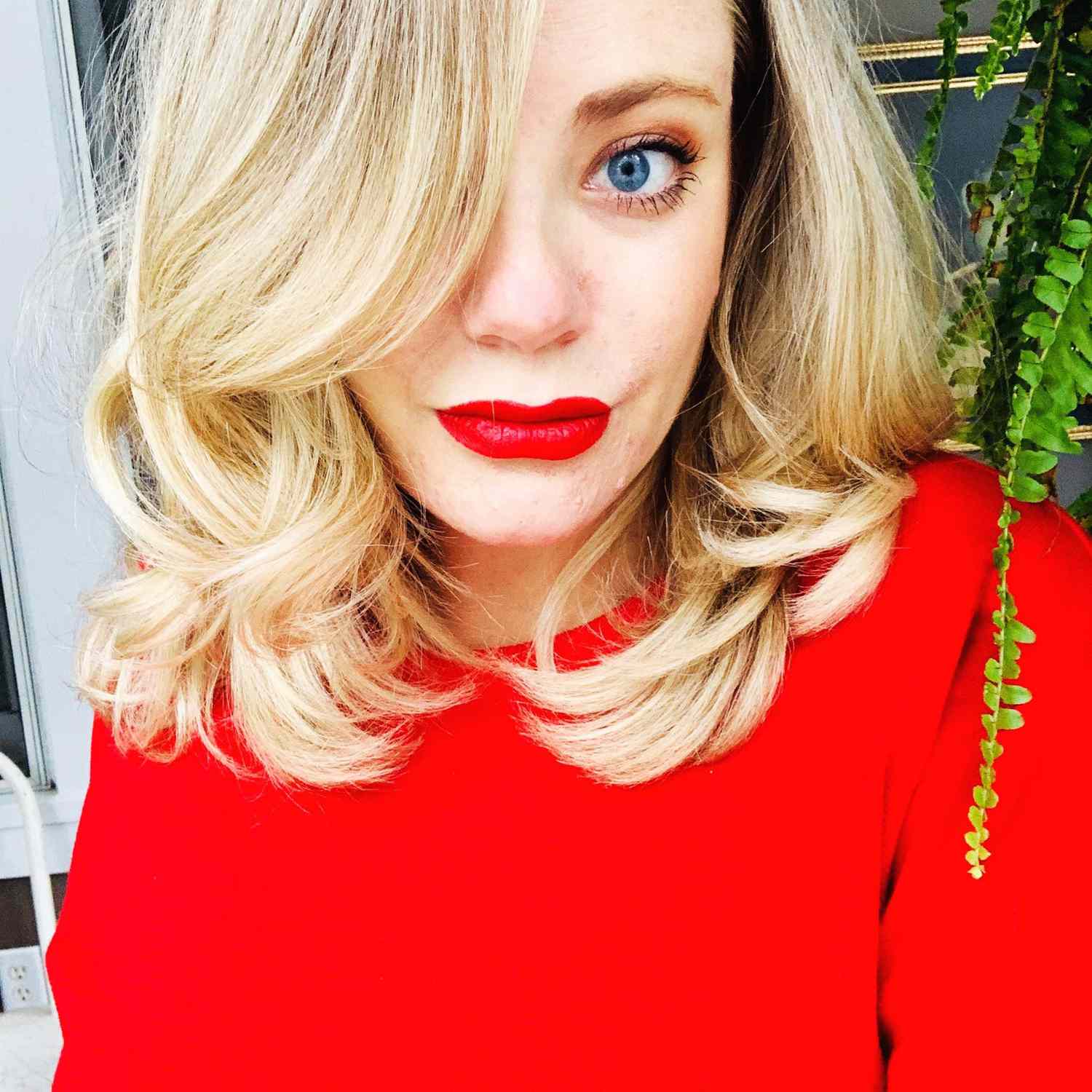 A photo of writer Kara Nesvig in a red sweater and red lipstick.