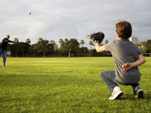 A grandfather throws a baseball to his grandson in a park