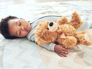婴儿穿着连体衣和泰迪熊睡在床上