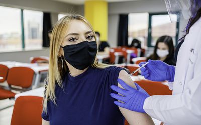 一个十几岁的女孩正在从护士那里接种疫苗＂width=
