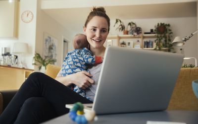 她在家里用笔记本电脑，抱着她刚出生的孩子