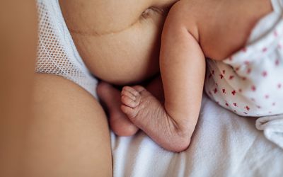 新生儿的腿特写，紧挨着妈妈的肚子和腿