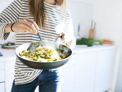 Young woman holding pan with vegan pasta dish