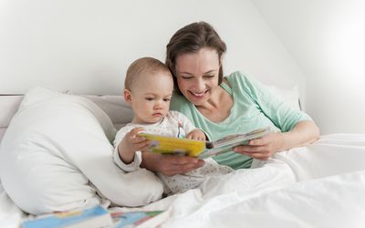 妈妈和宝宝在床上看绘本＂width=