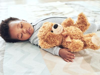 Baby wearing onesie sleeping on bed with teddy bear