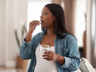 Pregnant woman drinking a glass of water and taking a pill.