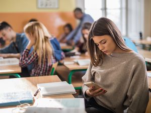 Female high school students using mobile phone during the class.