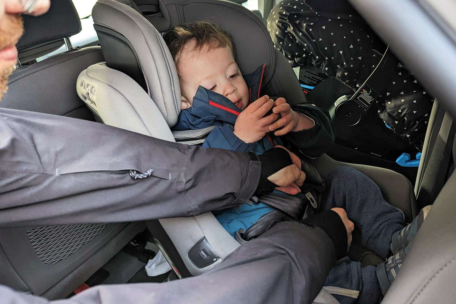 Person securing their child in the Nuna Rava Convertible Car Seat