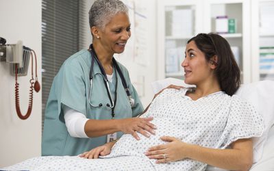 A pregnant woman in a hospital gown talking to her doctor in the hospital