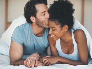 一名深情的中年男子在家里的床上放松时亲吻妻子的额头。