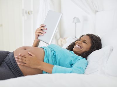 Pregnant woman in bed reading a tablet