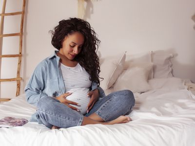pregnant person sitting in bed holding their belly