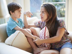 mother sternly talking to young son on couch