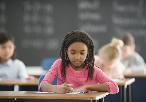 一个女学生在其他孩子的教室的桌子上写字