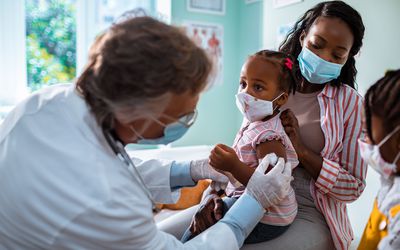 Pediatrician giving a young child a vaccination as her mother and sister looks on