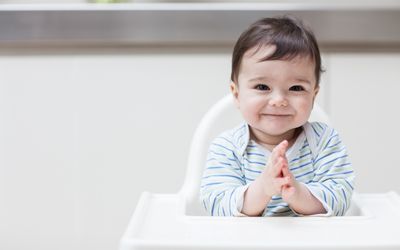 Baby boy in striped clothing sitting in high chair and clapping hands together