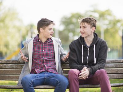 Two young male friends chatting on park bench