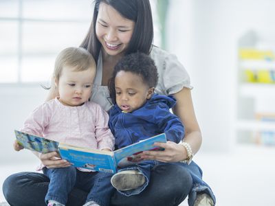 A preschool teacher reading to two toddlers