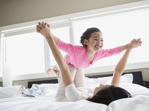 Girl playing airplane with mom on a bed