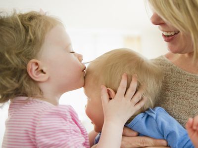 A little girl kissing her baby brother, who is held by their mom