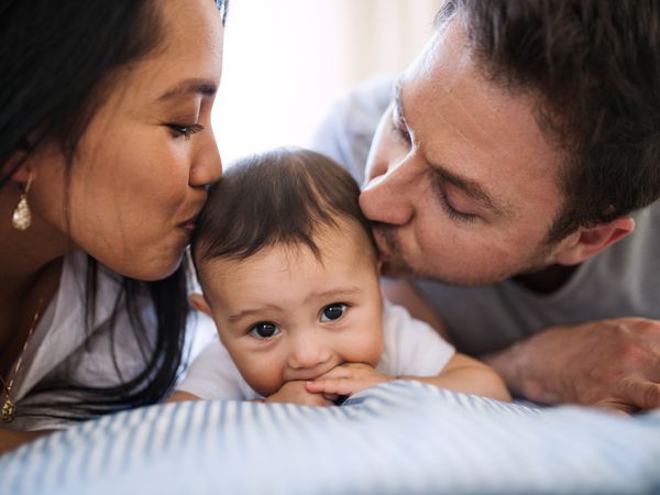 热情洋溢的年轻夫妇抱着一个婴儿在家里的床上休息。