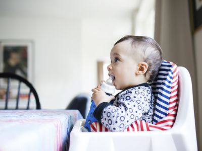 Baby drinking from bottle while sitting in high chair