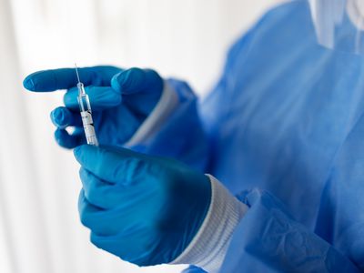 Close-up of a doctor hand wearing protective gloves preparing coronavirus vaccine syringe. Healthcare worker with a vaccination injection.